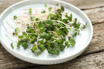 Plate with cut fresh radish microgreens on wooden table, closeup