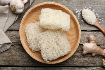 Bowl with dried rice noodles and ingredients on wooden table, flat lay