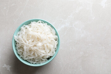 Bowl of tasty cooked rice noodles on light grey table, top view. Space for text