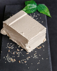 A large piece of sesame halva lies on a black serving board, a piece is cut off from the whole. National sweets, organic desserts concept 