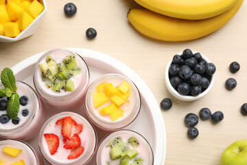 Yogurt maker with jars and different fruits on wooden table, flat lay