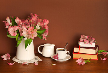 Morning still life with cup of coffee, books and flowers. Beautiful composition with bouquet of pink alstroemeria flowers in vase, porcelain white breakfastware and stack of old favorite books 