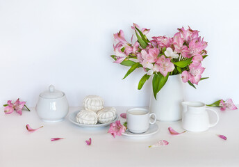 Beautiful still life with cup of milk, sweet marshmallows and a bouquet of pink fresh alstroemeria flowers in a vase on a white background. High key style. Festive afternoon tea. Holiday rest concept