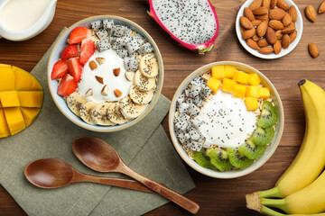 Bowls of granola with yogurt and fruits on wooden table, flat lay