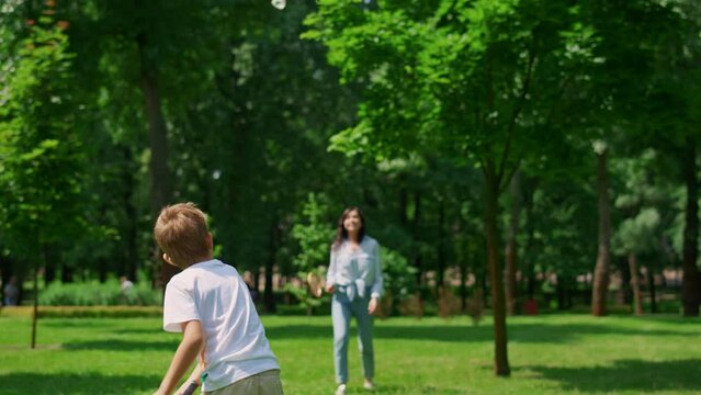 Joyful mother play badminton with son in park. Happy family have fun outdoor.
