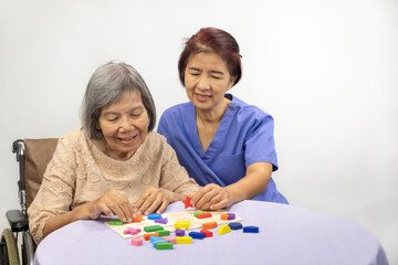 Obraz na płótnie Canvas Caregiver and senior woman playing wooden shape puzzles game for dementia prevention