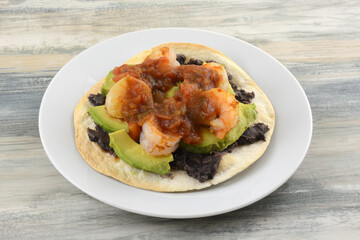 Shrimp and black bean tostada with avocado and salsa on white plate