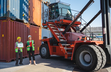 Female engineer and foreman standing at stacking forklift preparing import export goods at shipping terminal. Senior worker holds notebook checking containers loading data. Container handler concept.