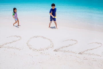 Two little kids writing 2022 numbers on beach