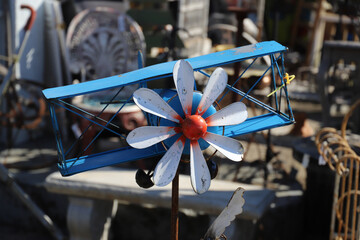 a blue biplane with a white and red propeller in the front on top of a rust metal rod surrounded by various antiques in Douglasville Georgia USA
