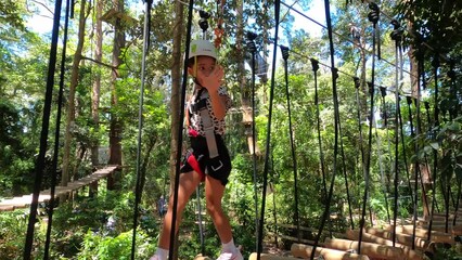 A young little girl walks across a bridge at a zipline adventure park for kids. Queensland Australia.