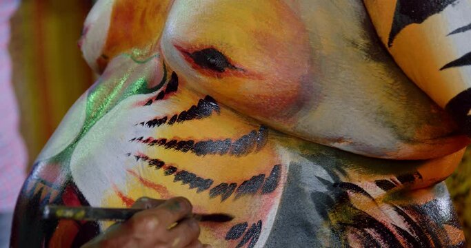 Artist painting tiger whiskers to the body art of a Pulikali performer - Tiger dance festival in Kerala, India. The Indian dance performer has the face of a tiger painted on his chest and belly.