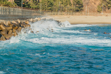 Waves surging against tetrapod breakwater on sunny winter morning.