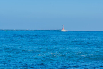 Red lighthouse on end of concrete pier in small fishing port.