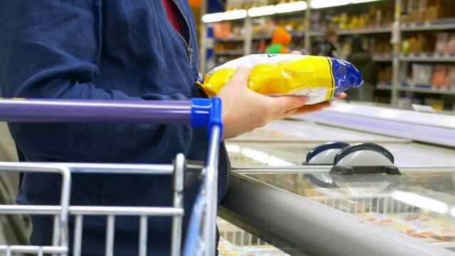 Shopping for groceries in a supermarket, a man takes out a frozen semi-finished product from the freezer and puts the purchase in a shopping cart. Buying frozen food in a man's choice store