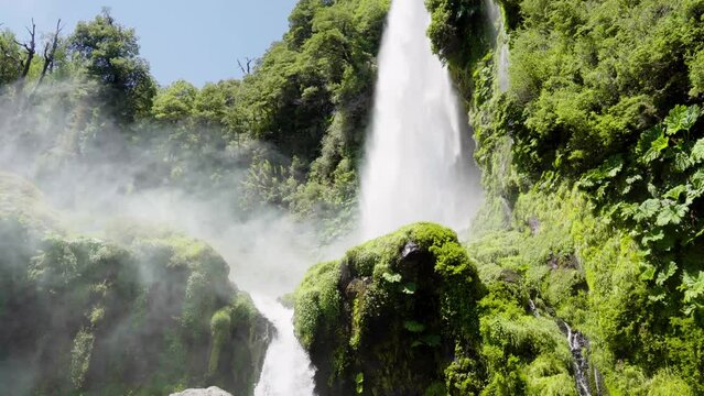 Pan left of Salto El Leon waterfall spraying water over rocks covered with moss in green rainforest near Pucon, Chile