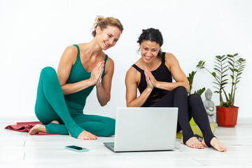 Two female yogi trainers have a video stream welcoming their subscribers while sitting on a mat in...