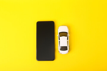 Toy car model with smartphone on yellow background.