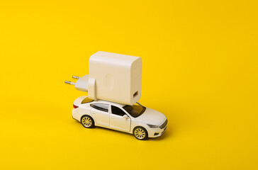 Toy model auto with charger on a yellow background. Electric car