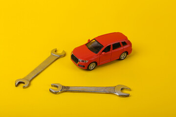 Toy car model with a wrench on a yellow background. Auto service, repair concept.