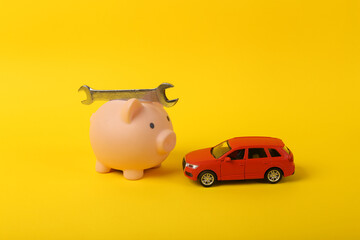 Toy car model with wrench and piggy bank on a yellow background. Auto service, repair concept.