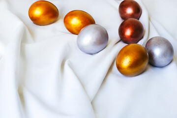 Easter eggs of golden and silver color lie on a white tablecloth.