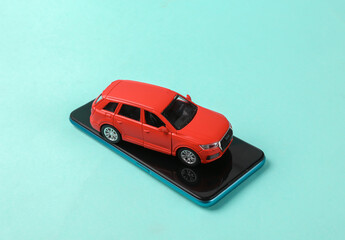 Toy car model with smartphone on blue background.