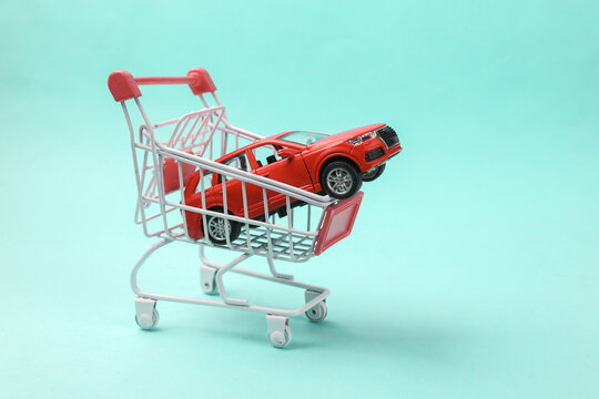 Buying car concept. Shopping cart with toy car model on blue background