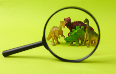 Toy dinosaurs magnified through magnifying glass on green background