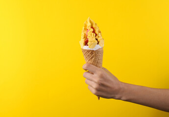 Female hand holds ce cream cone on a yellow background. Summer background