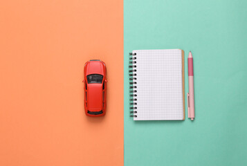 Fototapeta na wymiar Model toy car with notebook on blue-pink background. Top view. Flat lay