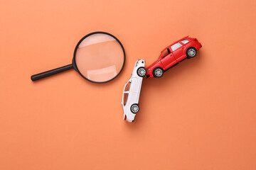 Two mini toy car crash and magnifying glass on coral color background, incident, car traffic accident - obrazy, fototapety, plakaty