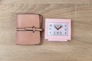 Square pink alarm clock with purse on wooden table