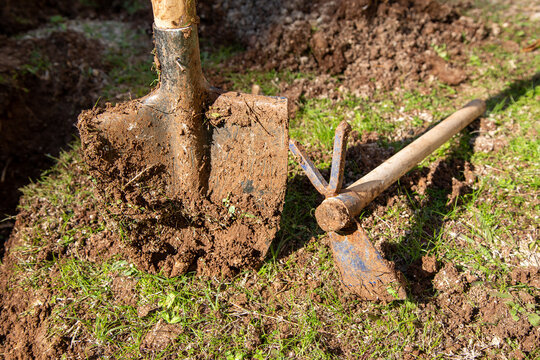 Used garden shovel and hoe with soil in selective focus. Farming shovel and hoe in daylight. Gardening, spring, agriculture concept.