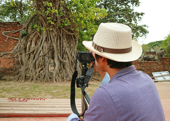 Visitor Taking Photos of the Famous Ancient Buddha Statue's Head Trapped in Bodhi Tree Roots in Wat Mahathat Temple Ruins, Ayutthaya, Thailand