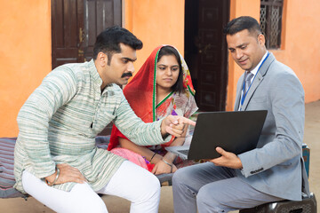 Bank person financial advisor showing scheme on laptop to rural Indian couple. 