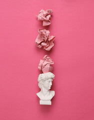 David bust with crumpled paper balls on pink background. Minimal layout
