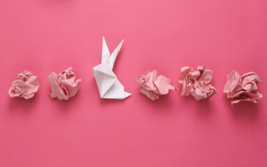 Crumpled pink paper with origami rabbit on pink background. Easter symbol