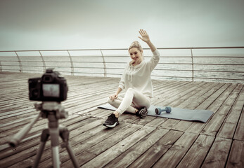 Fitness blogging. Young healthy sports woman recording herself on camera with tripod on the beach....