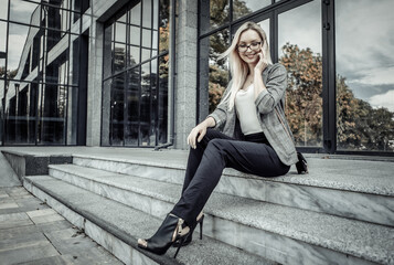 Happy Business woman sitting on the steps during the break and talking on phone on the background of a business center