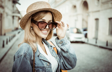 Street fashion, young stylish cheerful tourist woman in sunglasses and hat in the city