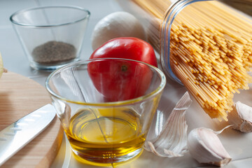 Raw, uncooked spaghetti with ingredients like tomato garlics, onion, olive oil, and black pepper with a round chopping board with a knife, horizontal image.