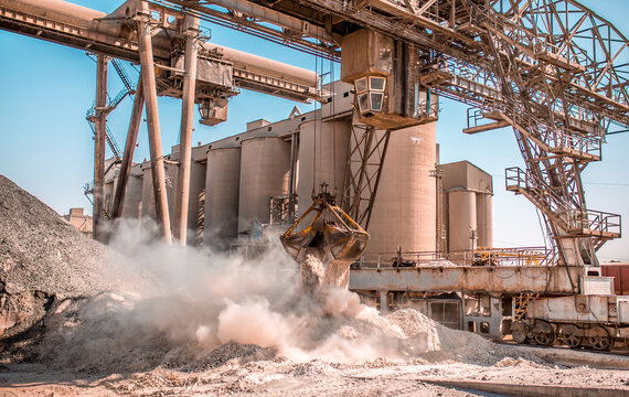 Modern technology of the bucket moves gravel, work at a cement plant. Technological work on the production of cement. Working atmosphere with copy space. Heaps of sand and soil raw materials.