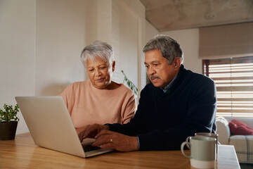 Elderly multi-ethnic couple researching holiday destinations on their laptop while sitting at home. Retired and happy.