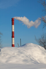 Obraz premium A smoking factory chimney against a clear blue sky and white snow