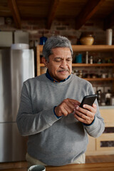 Portrait orientation of happy multi-cultural elderly male typing a message on smartphone while...