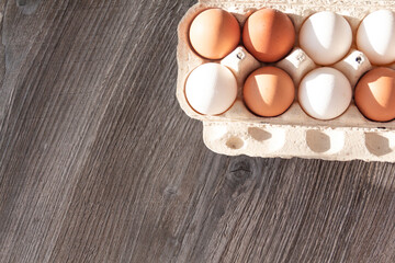 Chicken eggs are in a cardboard box on a wooden gray table.