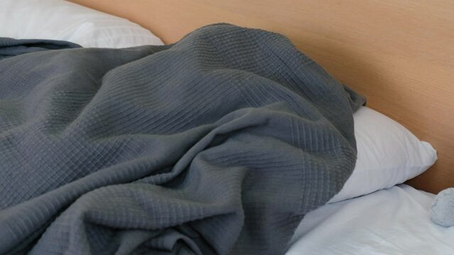 A disgruntled little boy with a fever is lying on the bed and hiding under the covers. High quality 4k footage
