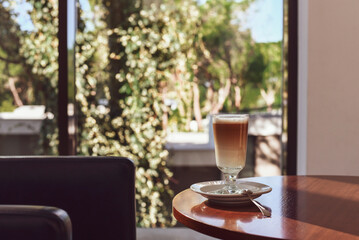 A cup of coffee on the table. It's sunny in the cafe. Large panoramic windows.
