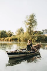 Foto op Canvas a young woman in a dress with bare shoulders sits in an old wooden boat on the lake. a woman is sailing in a boat with dry wildflowers and dry grass. a woman sits in a boat and dreams about something. © Anne Ponomarenko